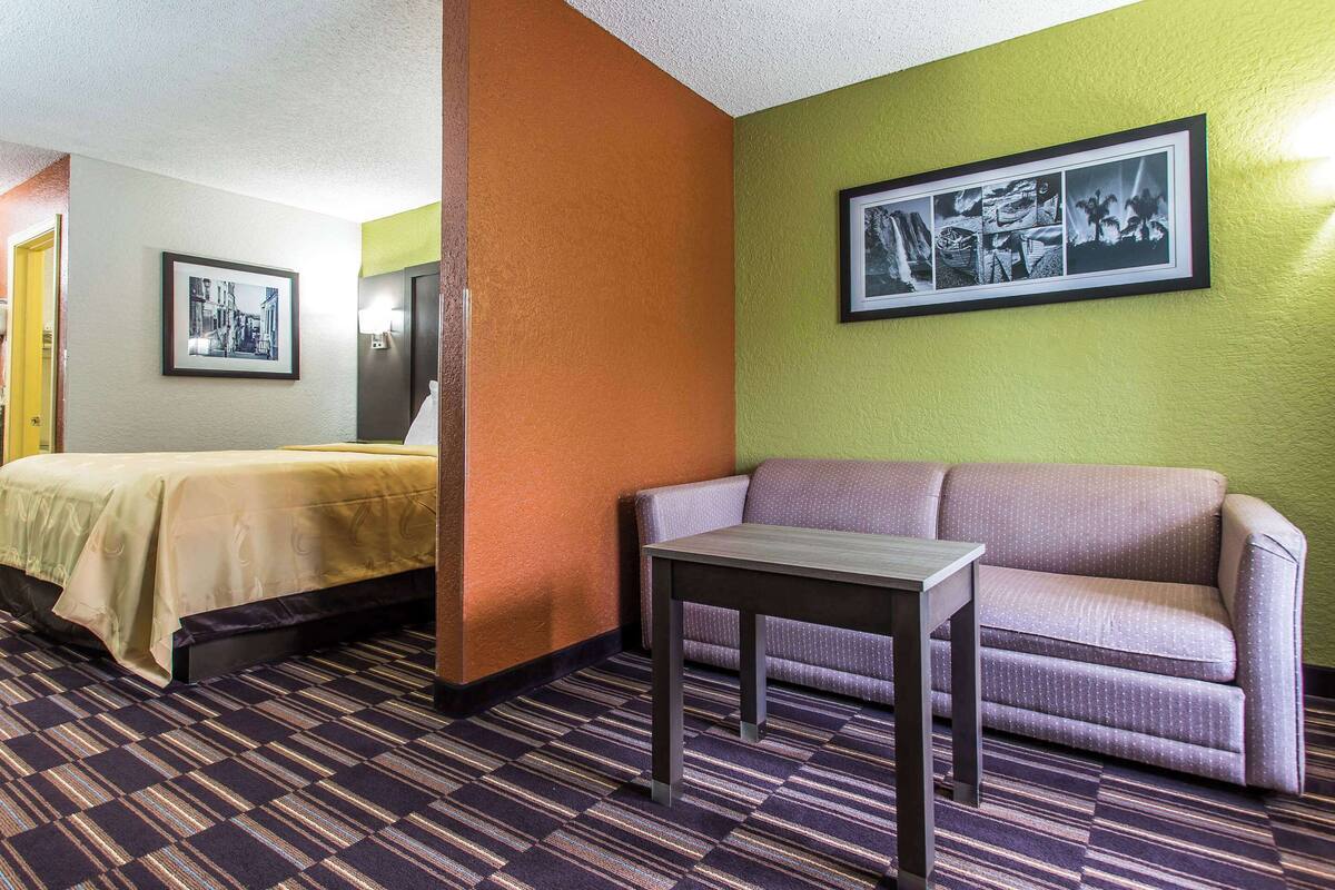 Habitación de hotel con cama, sofá, una mesita y un cuadro colgado en la pared.