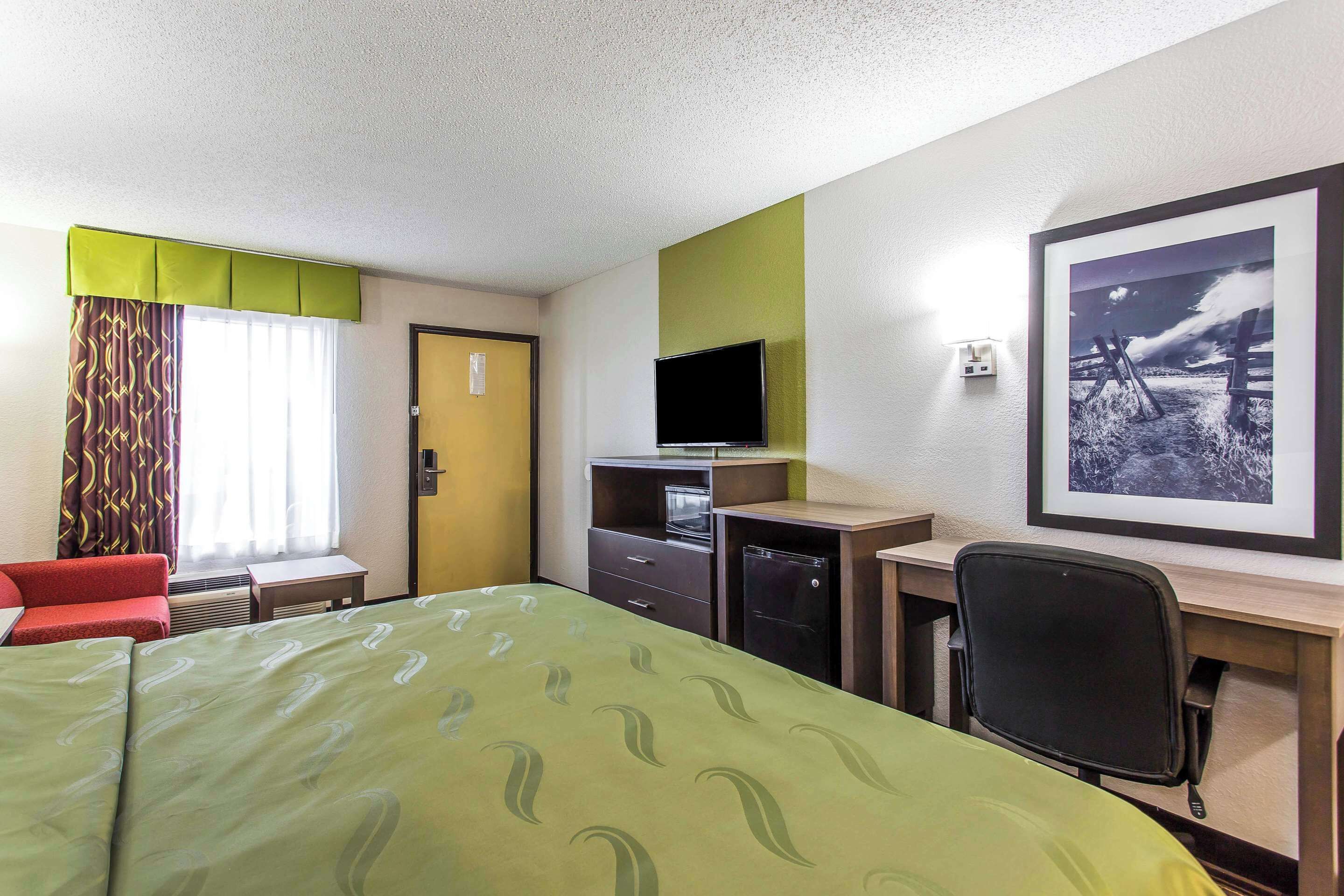A hotel room with a bed, a desk, a chair, a television, and a framed picture on the wall.