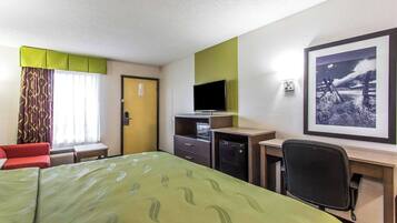 A hotel room with a bed, a desk, a chair, a television, and a framed picture on the wall.