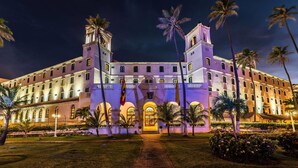 Un edificio grande y histórico con un patio central, palmeras y una entrada bien iluminada.