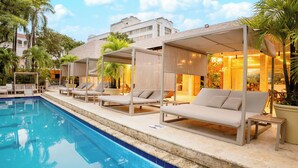 Un área junto a la piscina con sillones de descanso y una zona de estar techada.