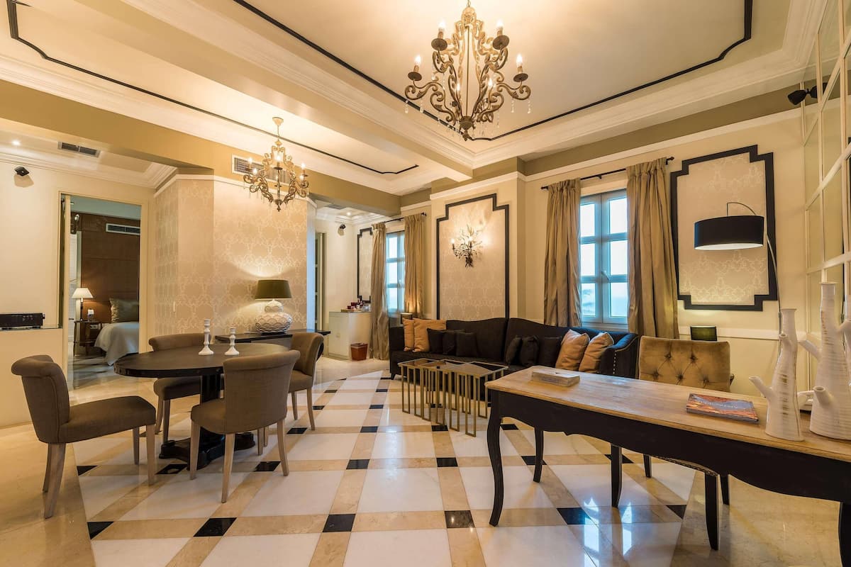 Een hotellobby met een zwart-wit schaakbordvloer, een ronde eettafel, banken en een kroonluchter.