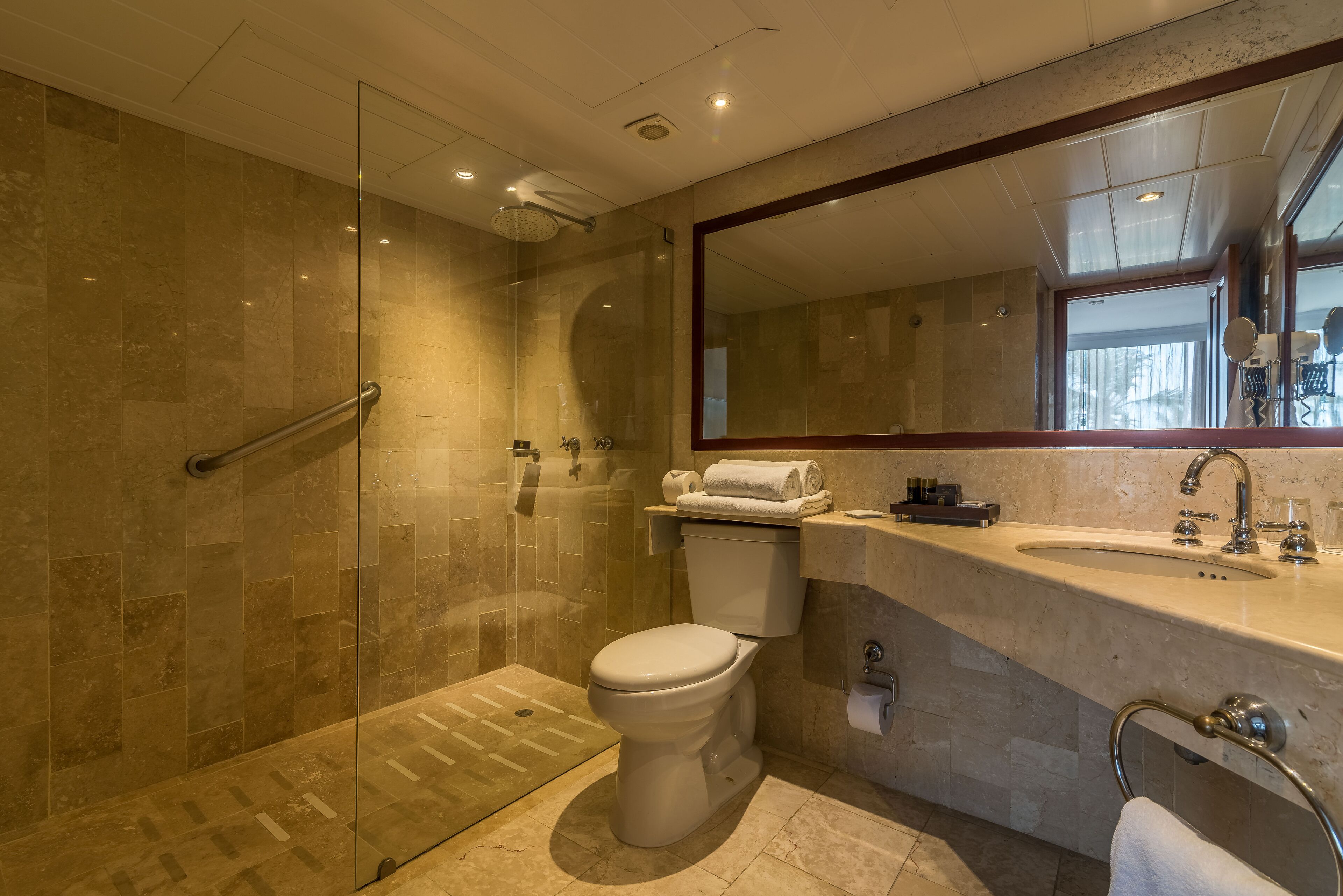 Un baño moderno con ducha de mampara de vidrio, inodoro y lavamanos con un espejo grande arriba.