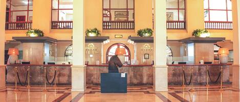 A hotel lobby with marble flooring, a reception desk, and a chandelier.