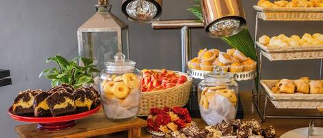 A buffet table with various baked goods, including muffins and pastries, arranged on a wooden table with metal stands.