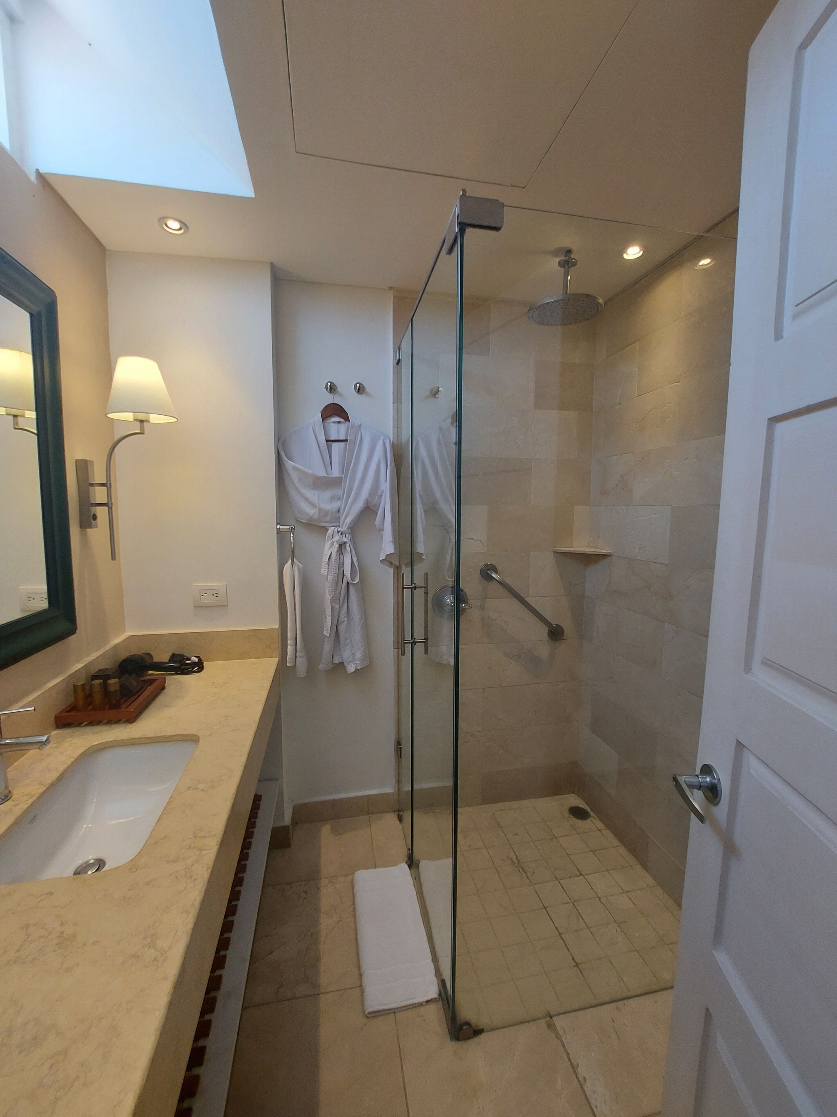 Un baño moderno con cabina de ducha acristalada, un lavabo con encimera de mármol y una bata colgada en la pared.