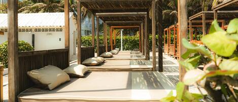 A series of wooden cabanas with cushioned seating and a thatched roof, surrounded by lush greenery.