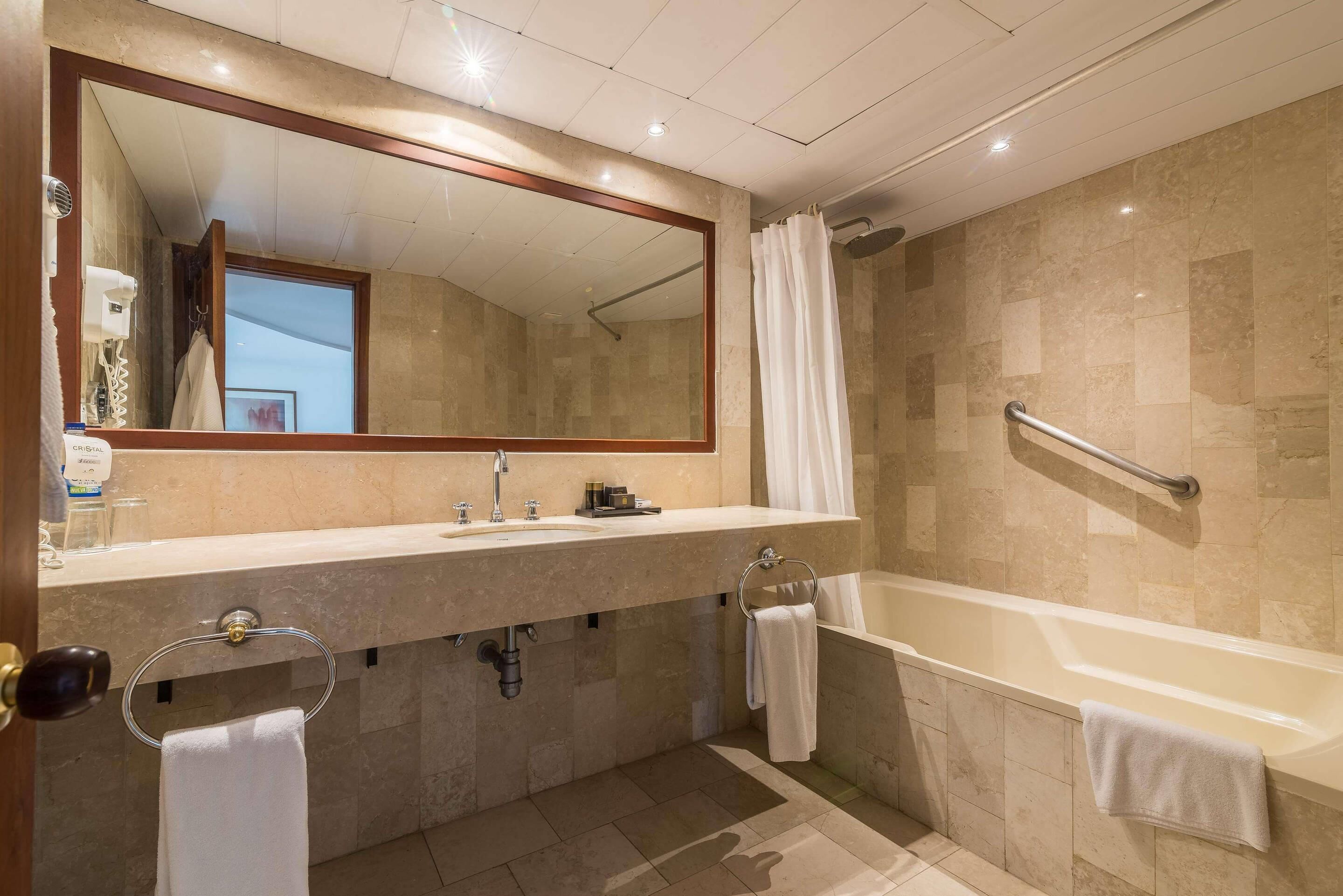 A modern bathroom with a large mirror, two sinks, a bathtub, and a shower.