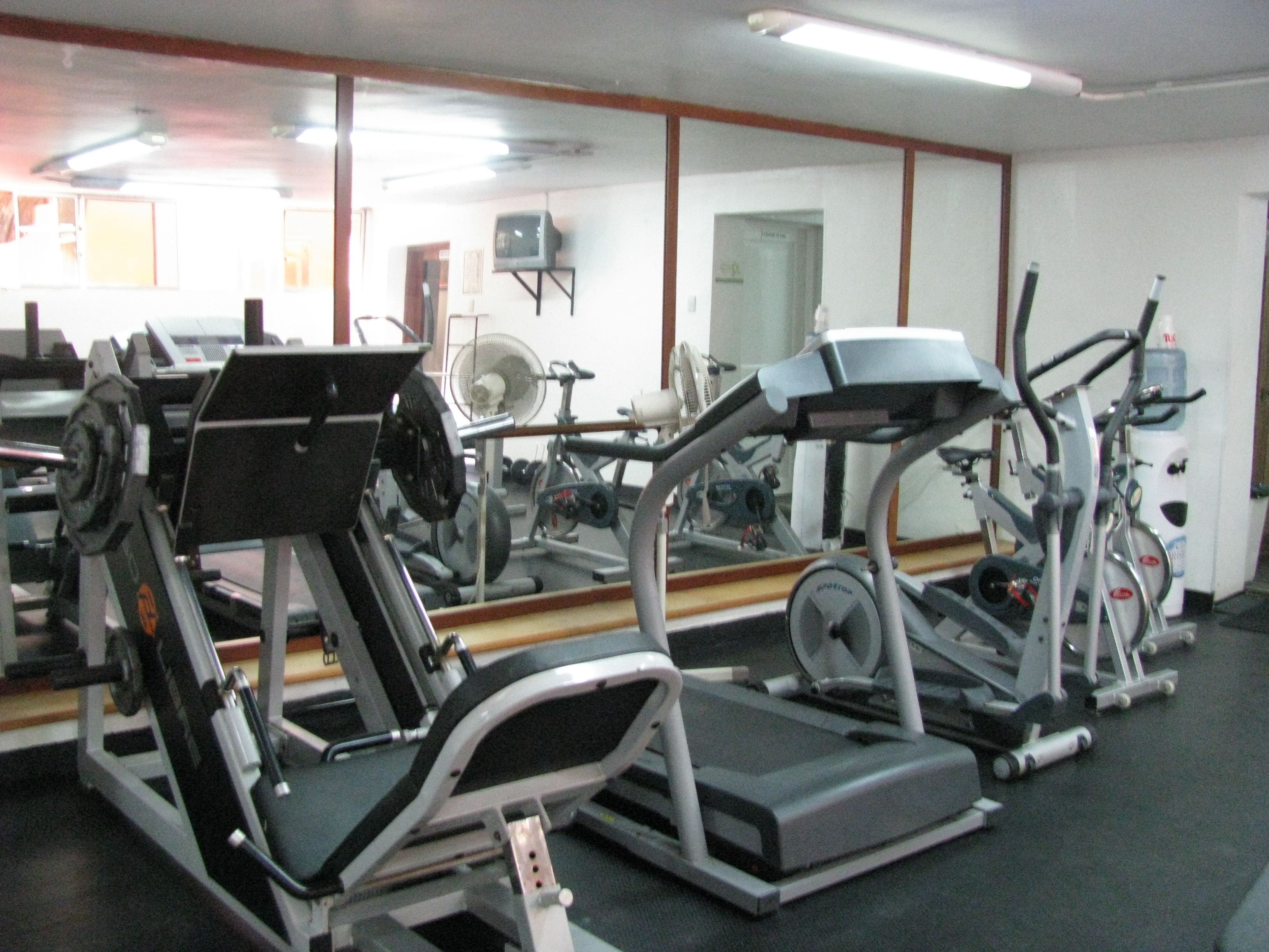 Un gimnasio con varios equipos de ejercicio, incluyendo cintas de correr, un banco de pesas y un ventilador.