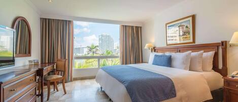 Habitación de hotel con una cama grande, un escritorio con silla, televisión y ventana con cortinas.