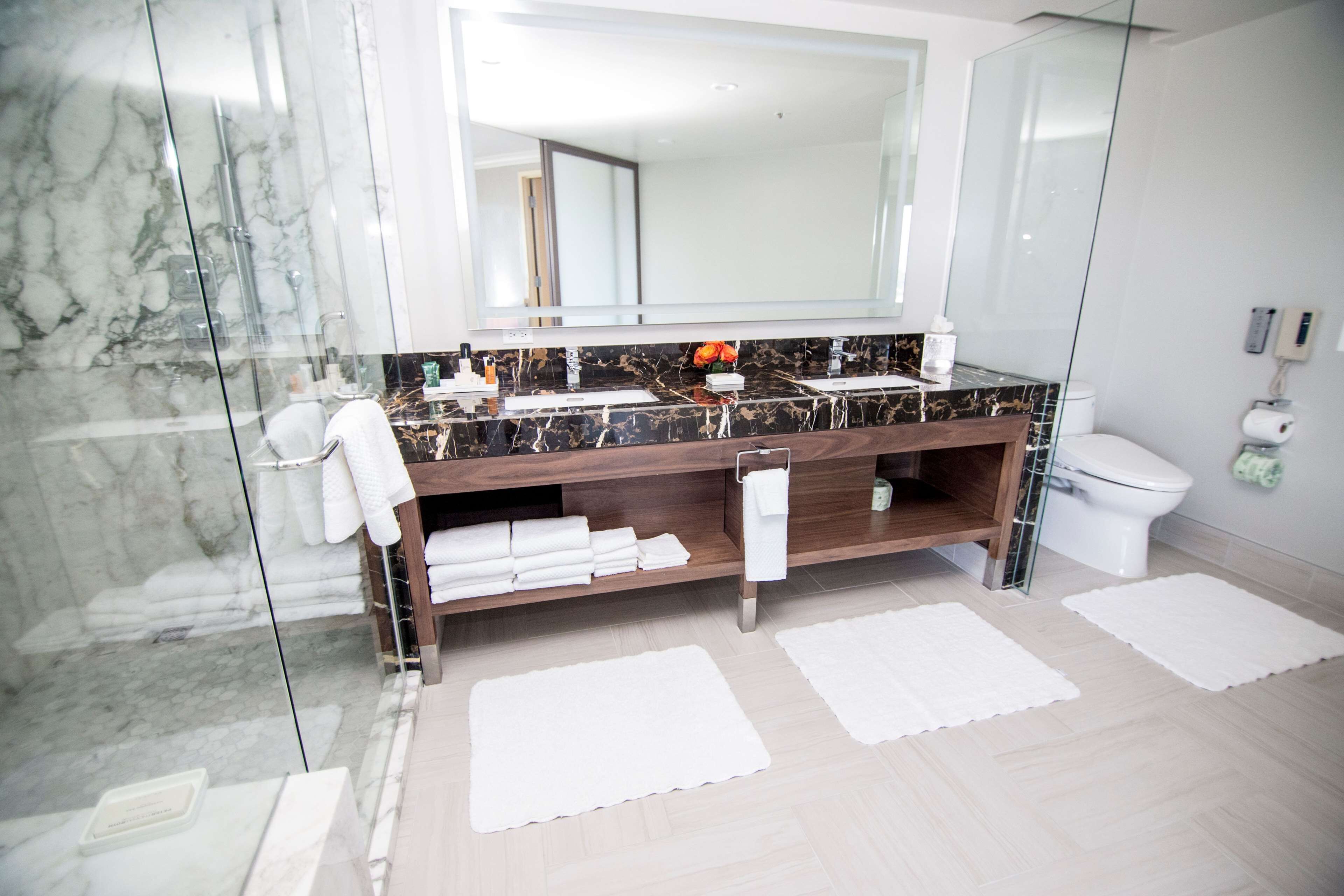 Un baño moderno con ducha de mármol, un espejo grande, un mueble de tocador de madera y un inodoro.