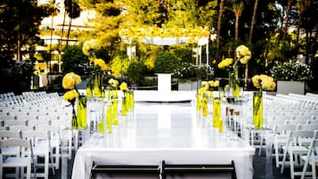 An outdoor wedding venue with rows of white chairs, a central aisle with yellow flowers, and a white altar.