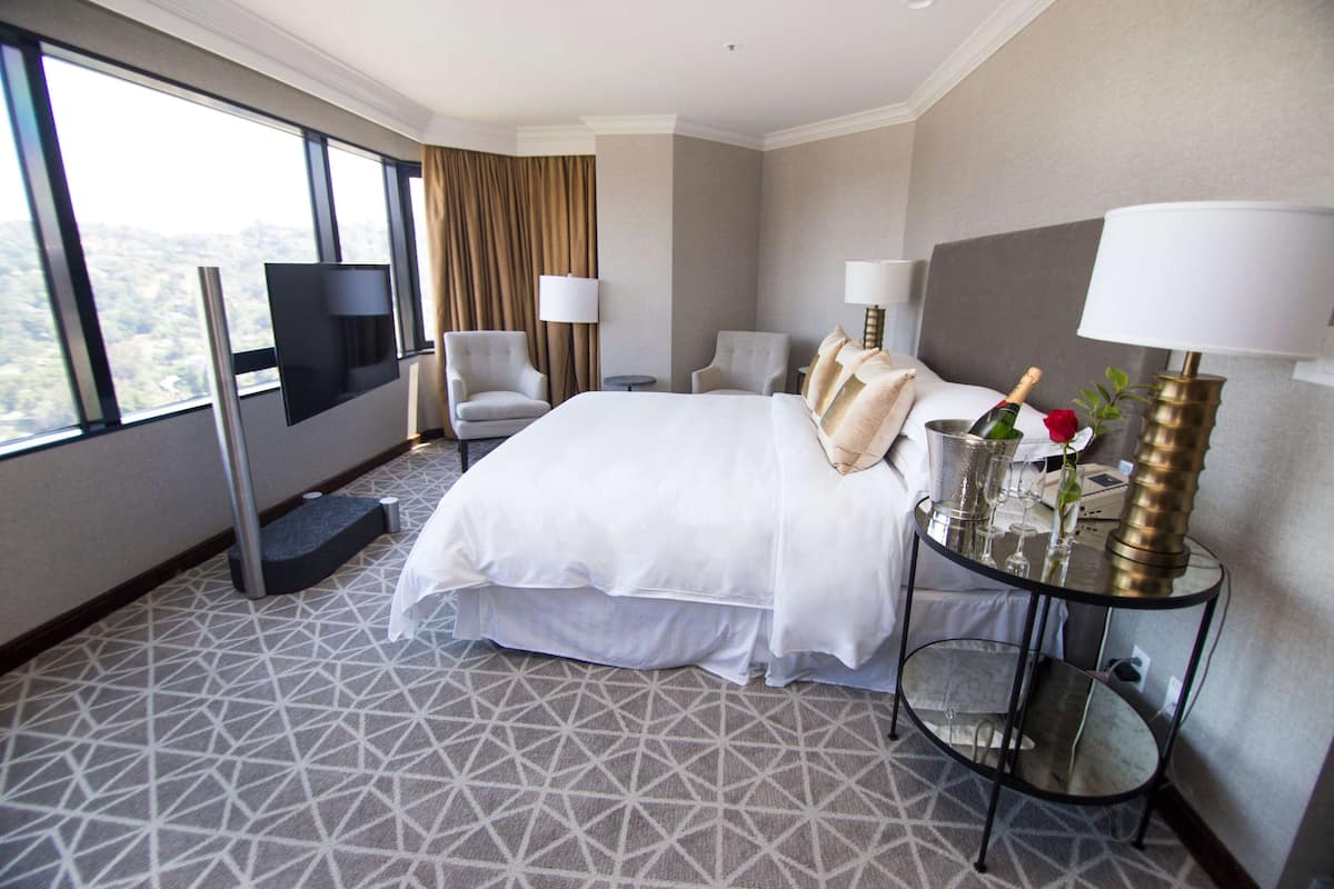 A hotel room with a large bed, two armchairs, a TV, and a table with a lamp and a bottle of champagne.