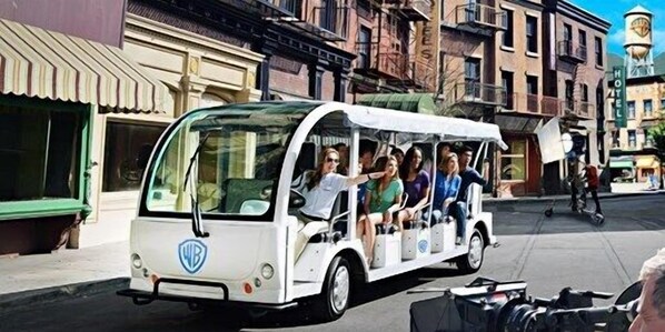 A white tour bus with passengers, parked on a street with buildings in the background.
