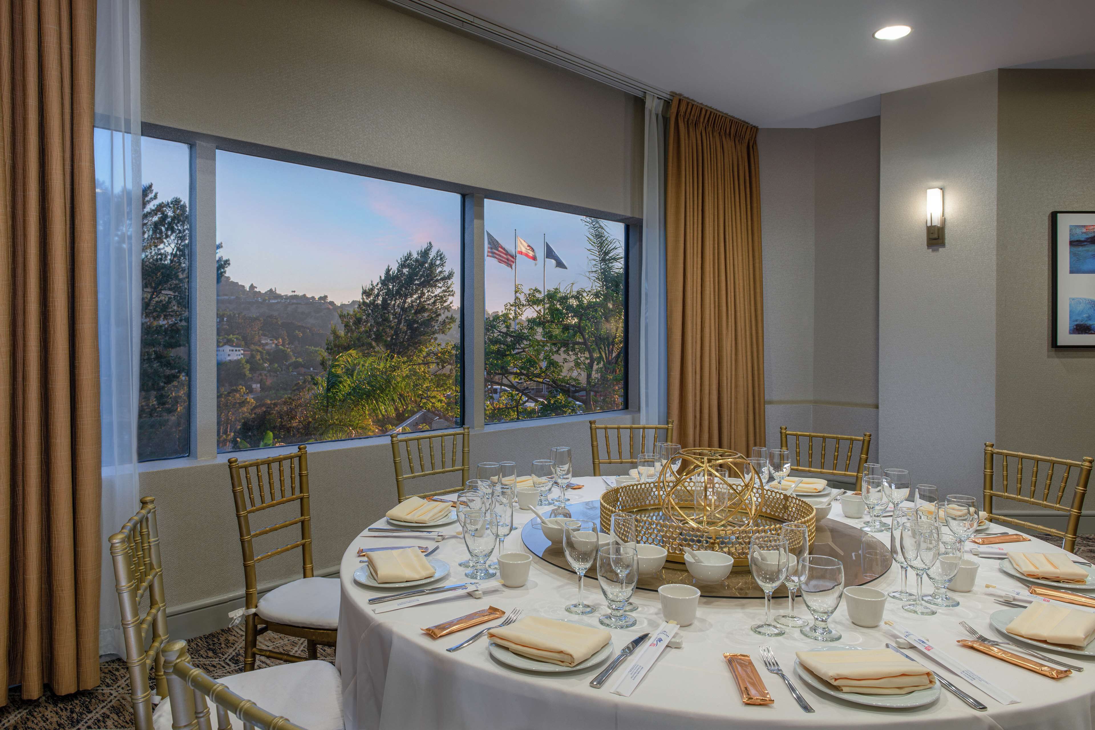 A dining room with a round table set for a meal, large windows with a view, and a chandelier centerpiece.