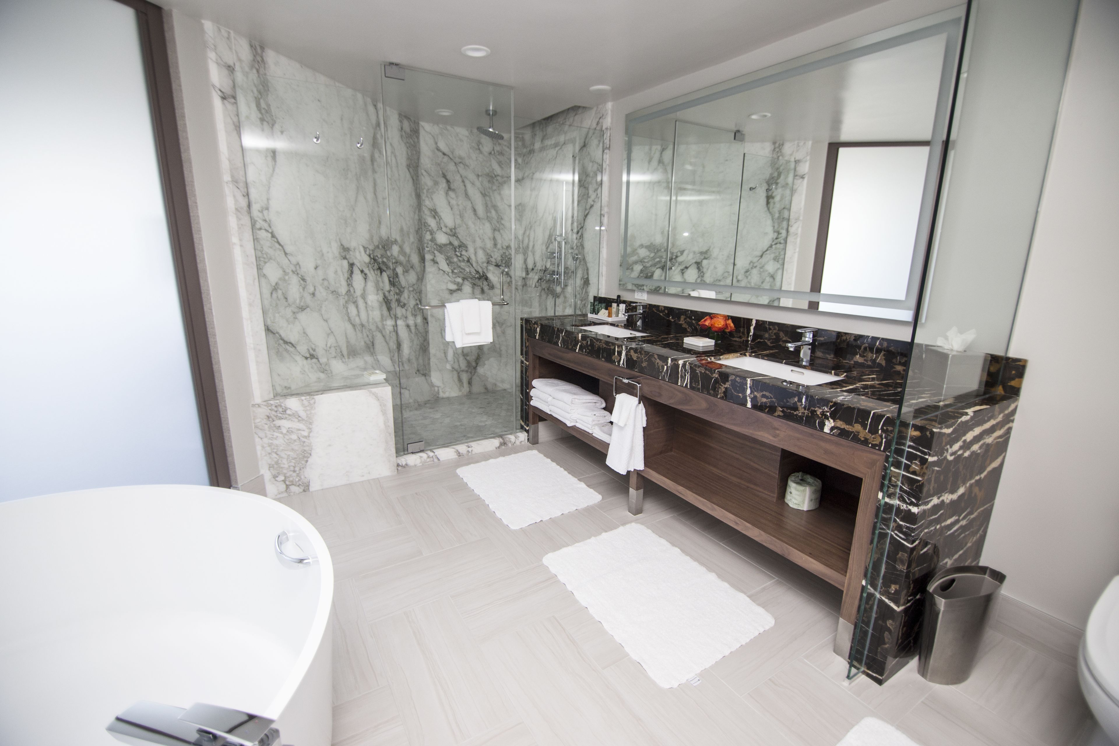 A modern bathroom with a marble shower, a large mirror, and a bathtub.