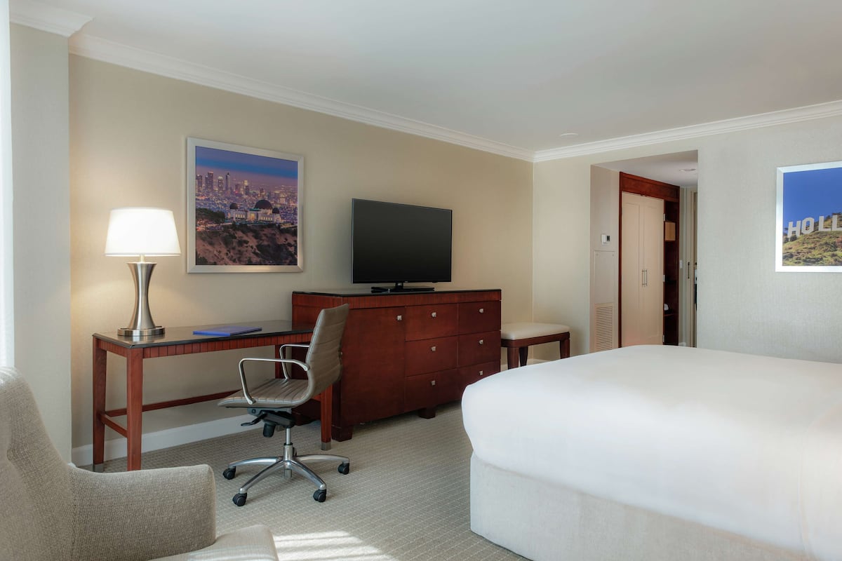 A hotel room with a bed, a desk with a lamp, a television, and a chair.