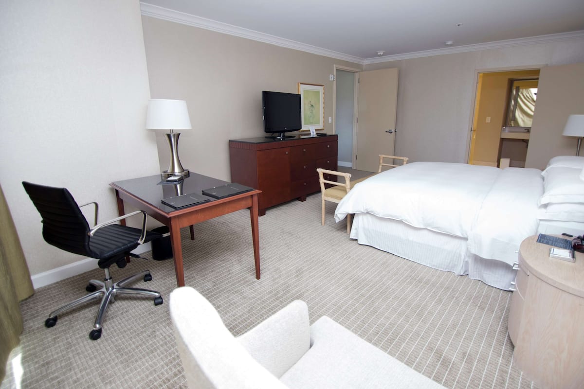 A hotel room with a bed, a desk with a chair, a dresser, a television, and a lamp.