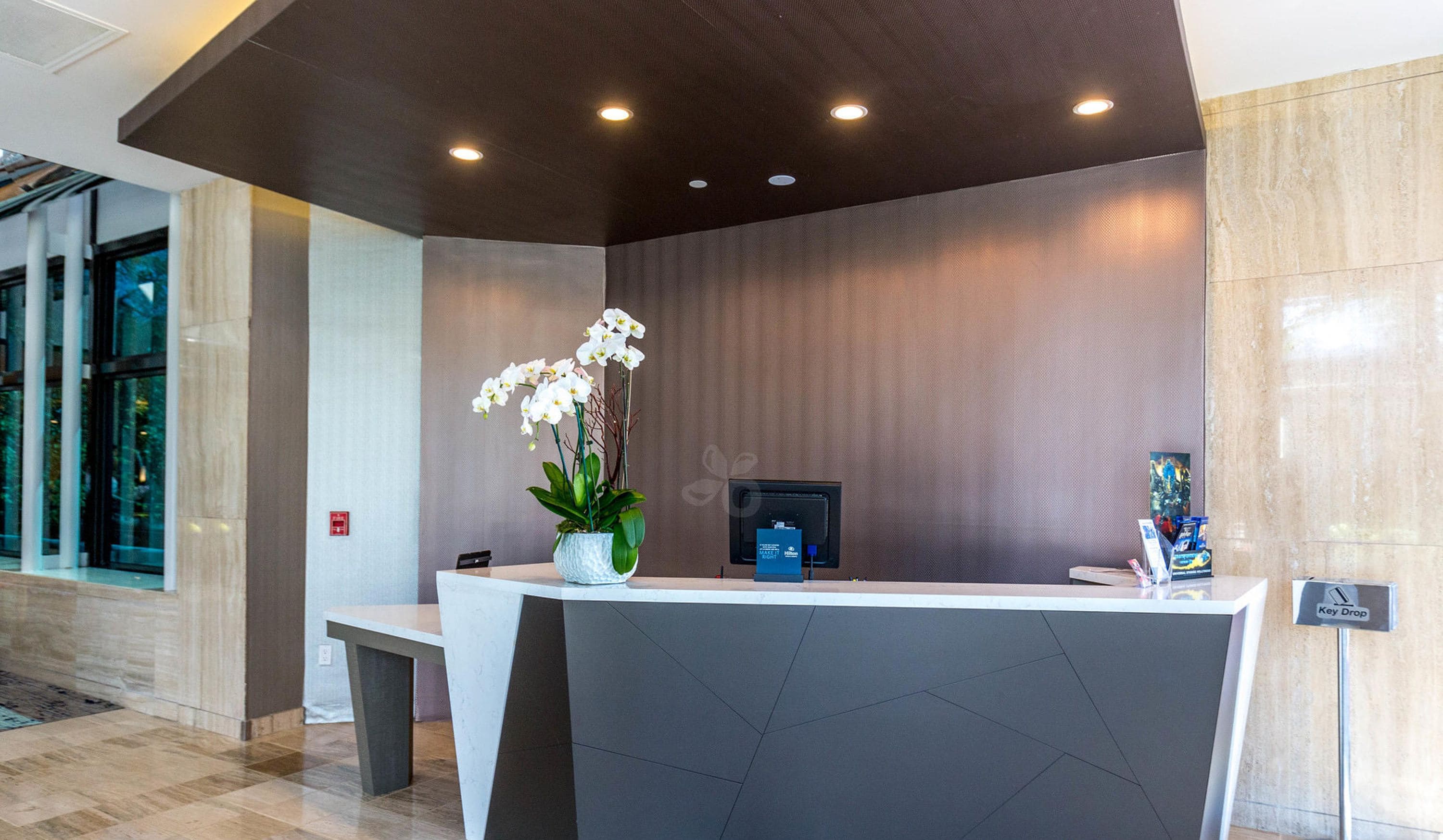 A reception desk with a vase of white orchids, a digital screen, and a key drop station.