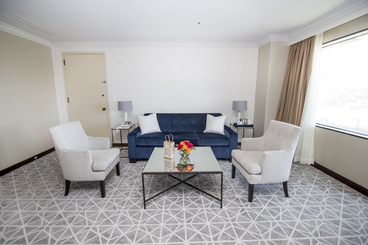 A hotel room with a blue sofa, two armchairs, a coffee table with a vase of flowers, and a patterned carpet.