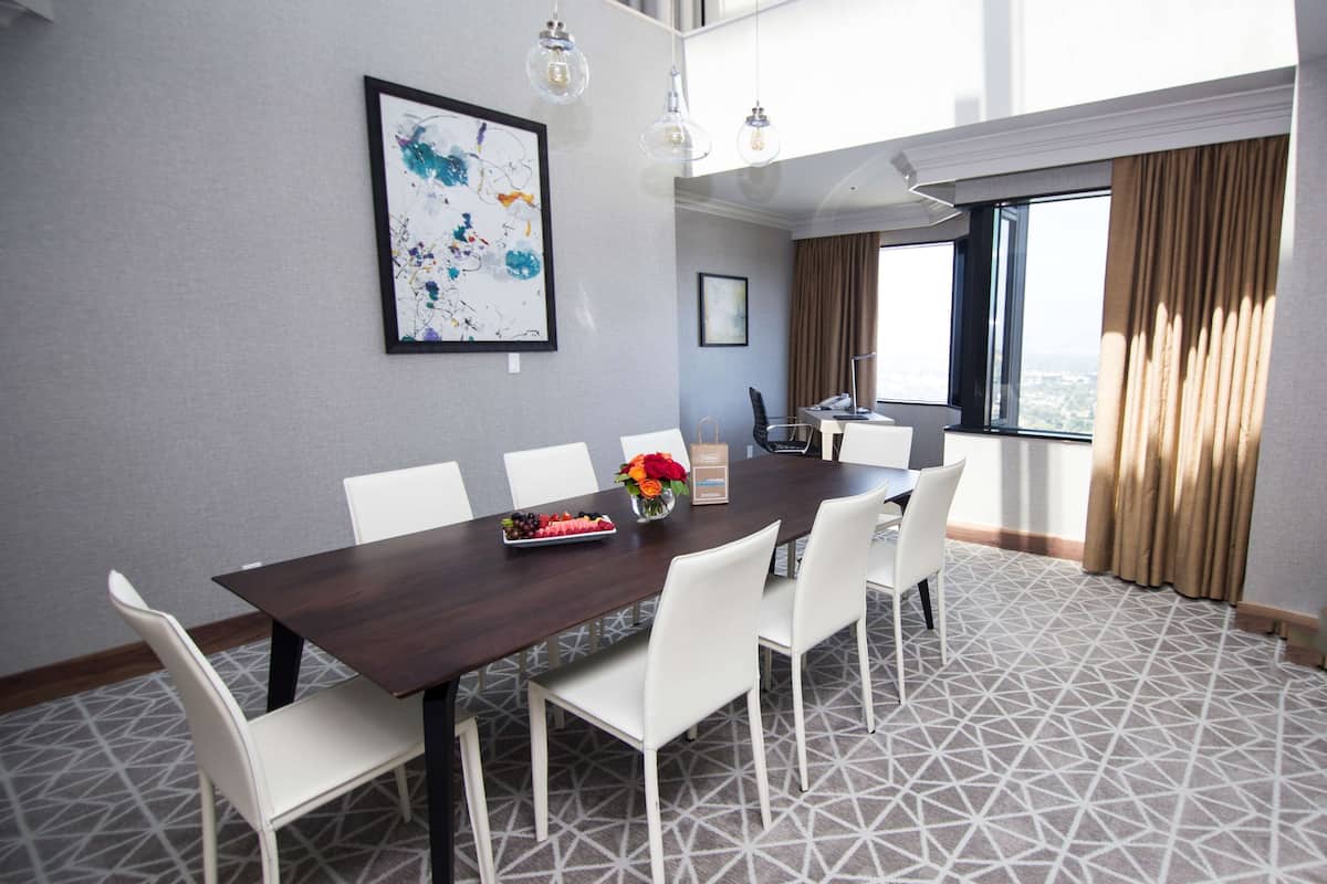 A conference room with a dark wooden table, white chairs, a framed abstract painting, and a vase with flowers.