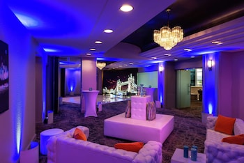 A long glass table with white chairs, surrounded by white floral arrangements, in a room with draped curtains and purple lighting. at Hilton Los Angeles/Universal City