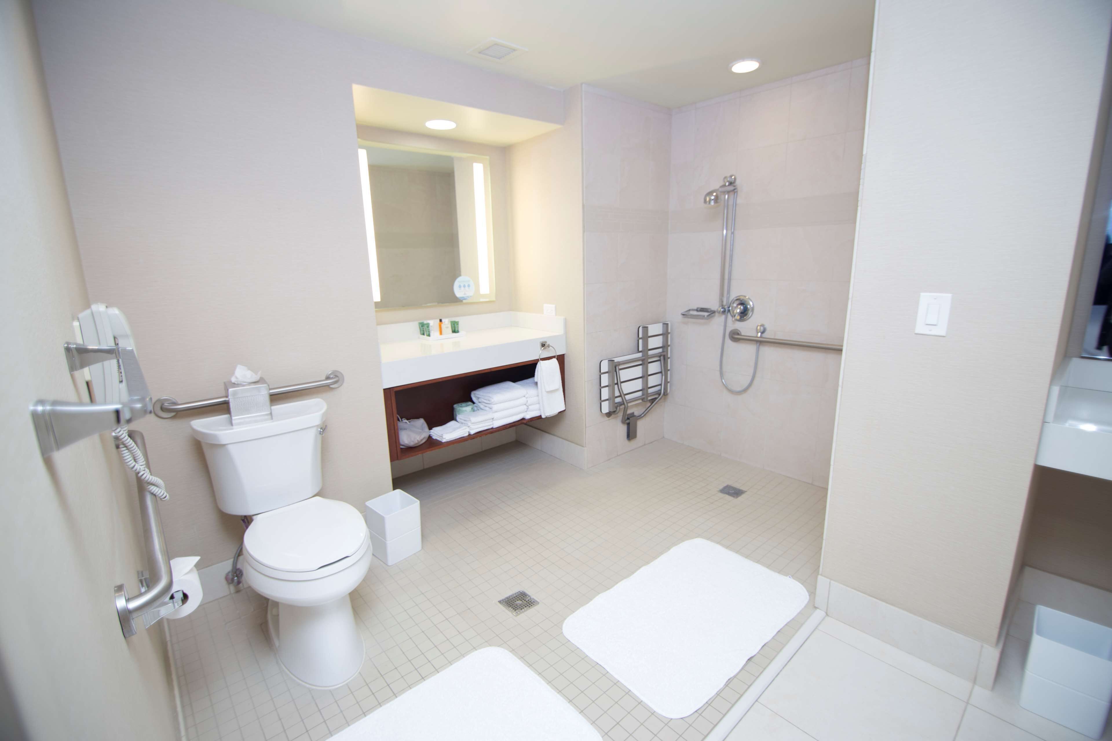 A modern bathroom with a toilet, sink, shower, and two white mats.