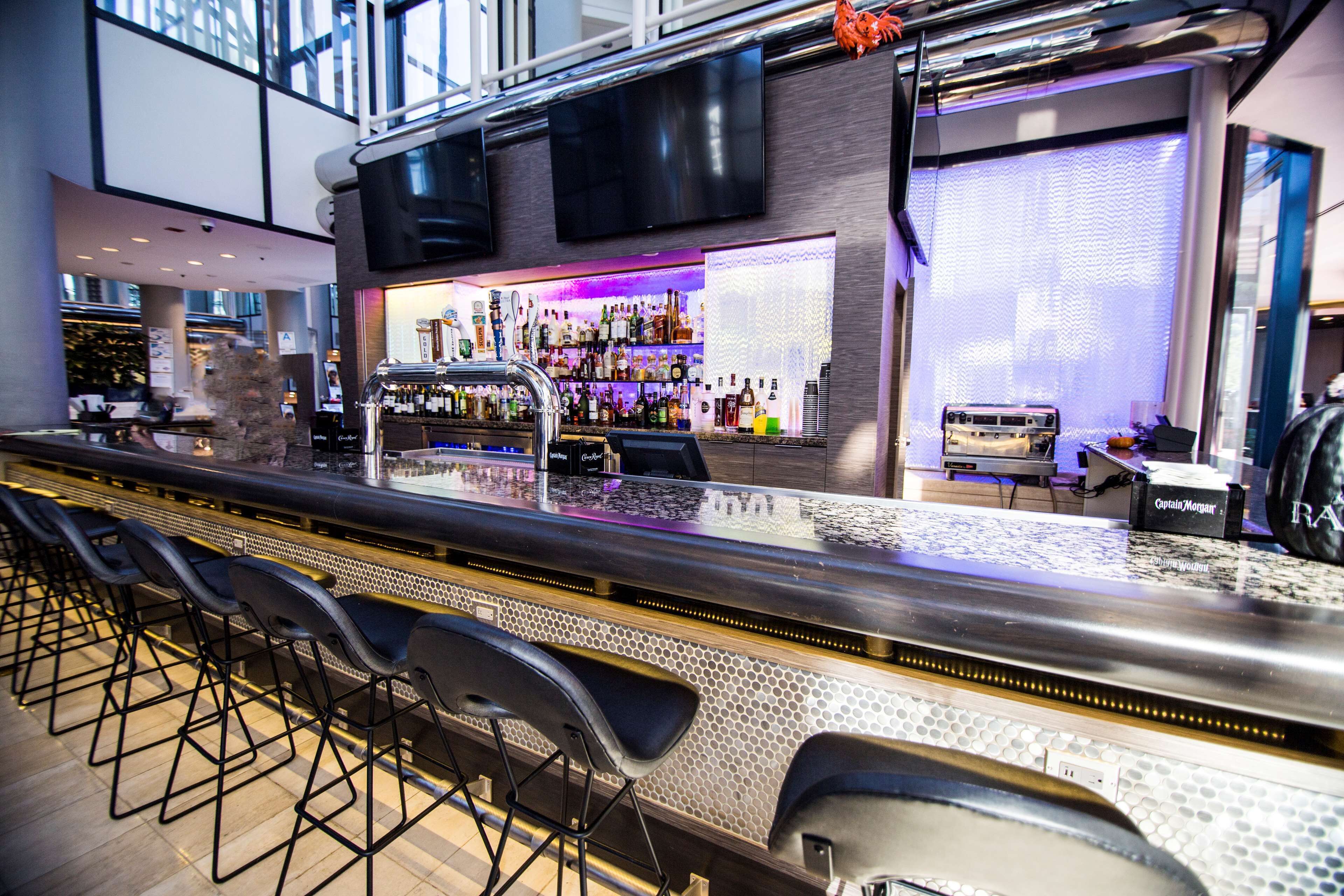 Una zona de bar con una barra larga, varios taburetes y una variedad de botellas y vasos.