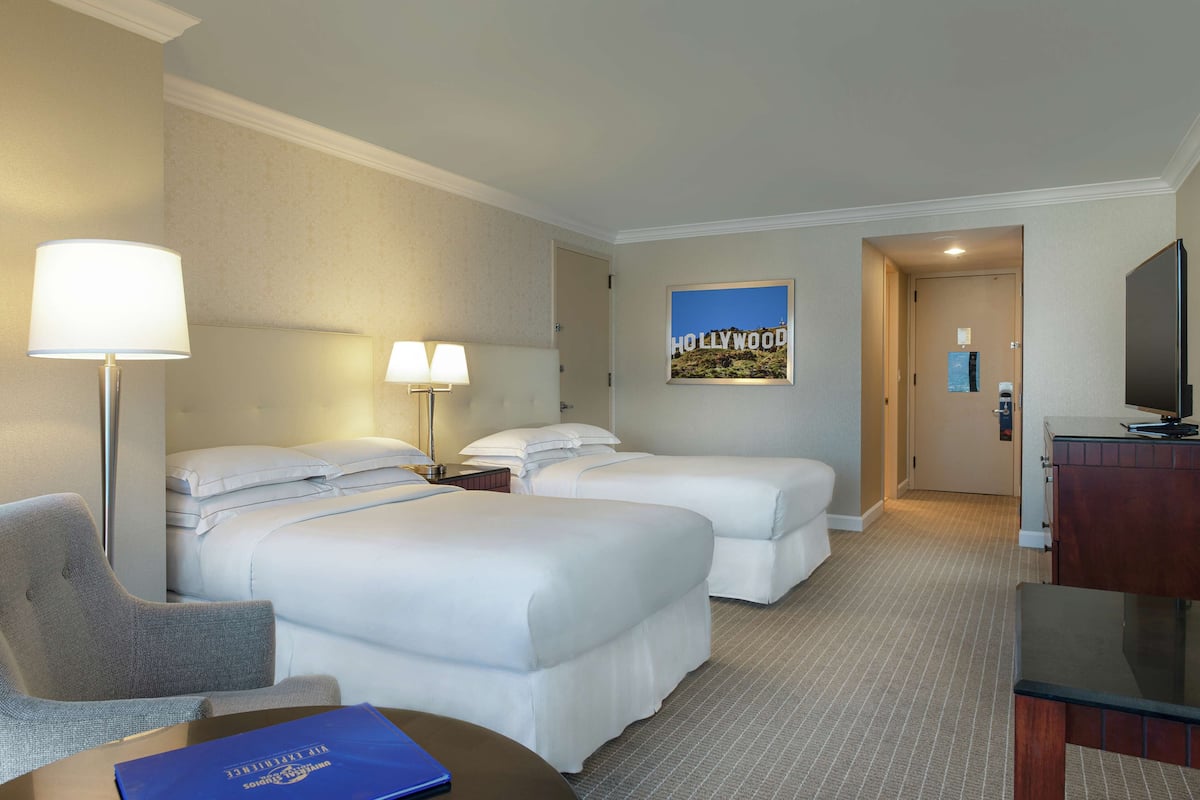 A hotel room with two beds, a desk with a lamp, a chair, and a television.