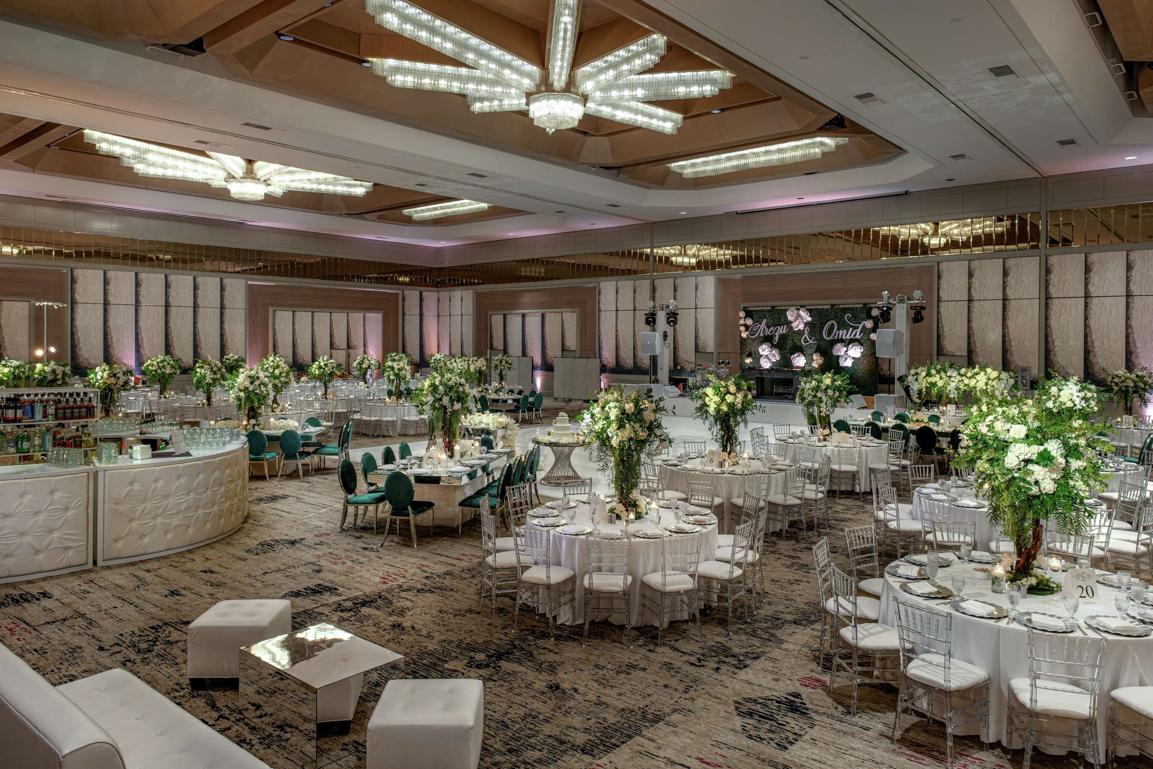 Une salle de banquet spacieuse, avec des tables rondes, des chaises blanches et des centres de table floraux.