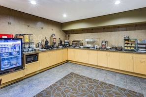 Een hotelkeuken met een ontbijtbuffet, inclusief een koelkast met drankjes, een koffieapparaat en diverse etenswaren.