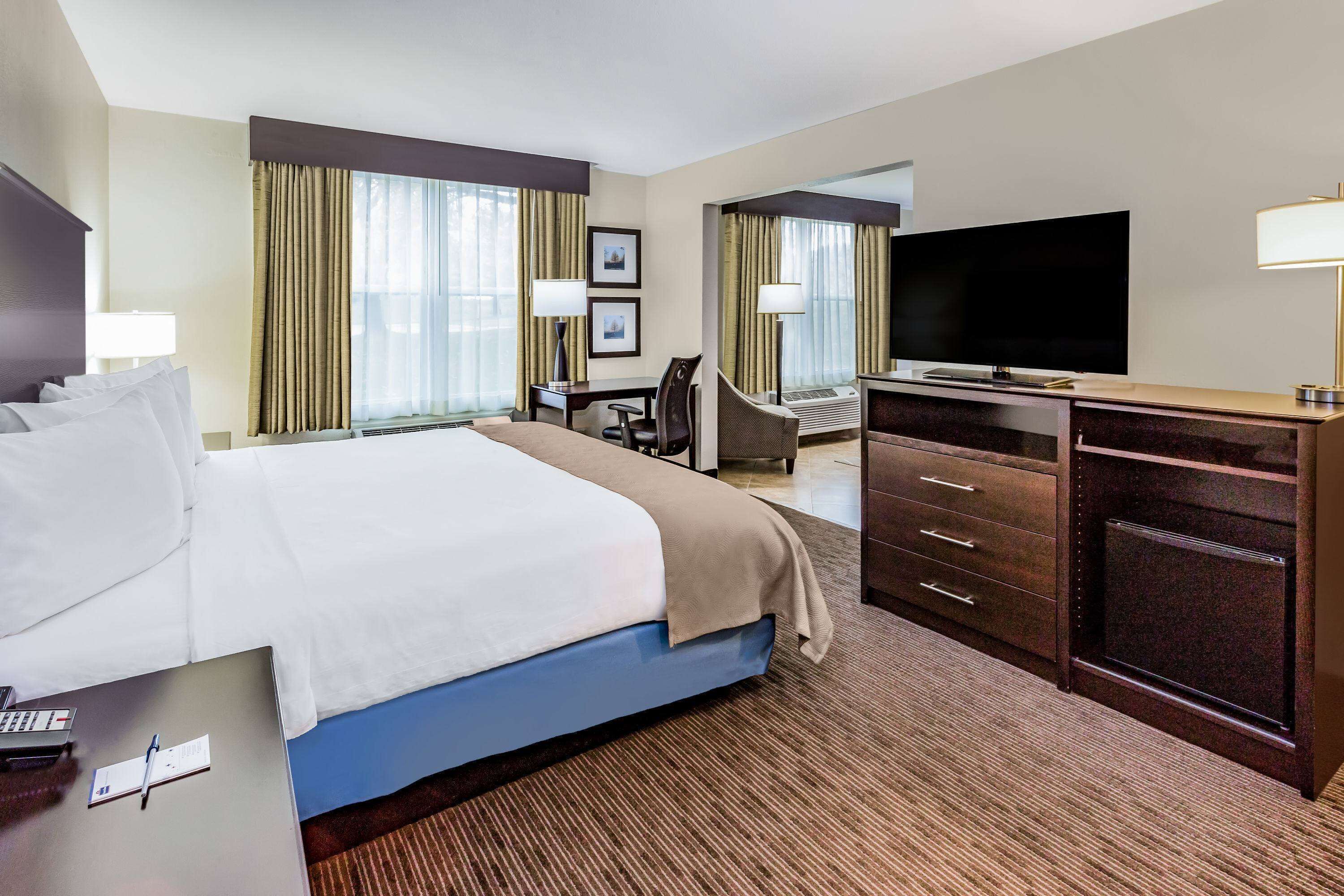 A hotel room with a large bed, a desk with a computer, a flat-screen TV, and a minibar.