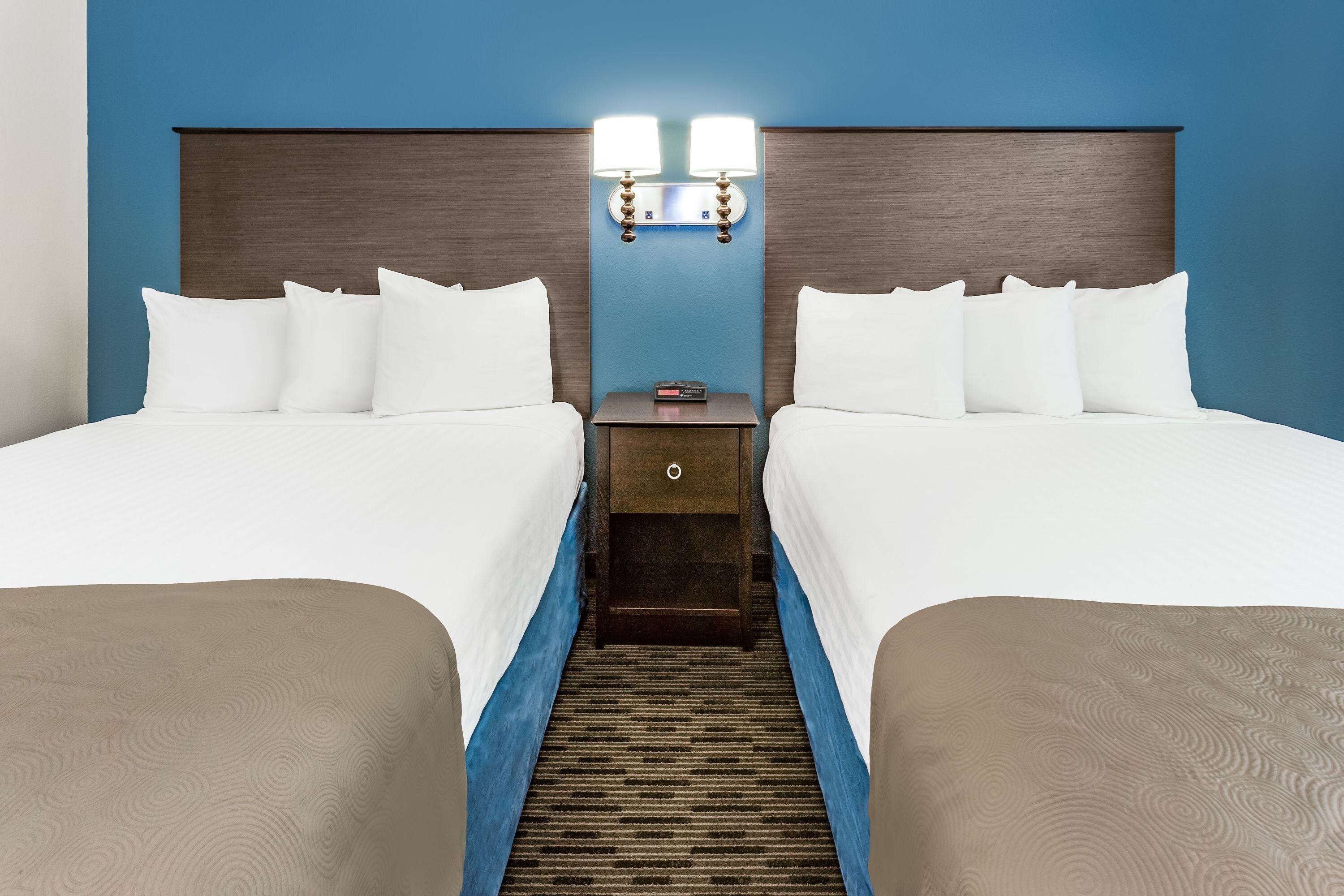 A hotel room with two beds, a nightstand, and a wall-mounted lamp.