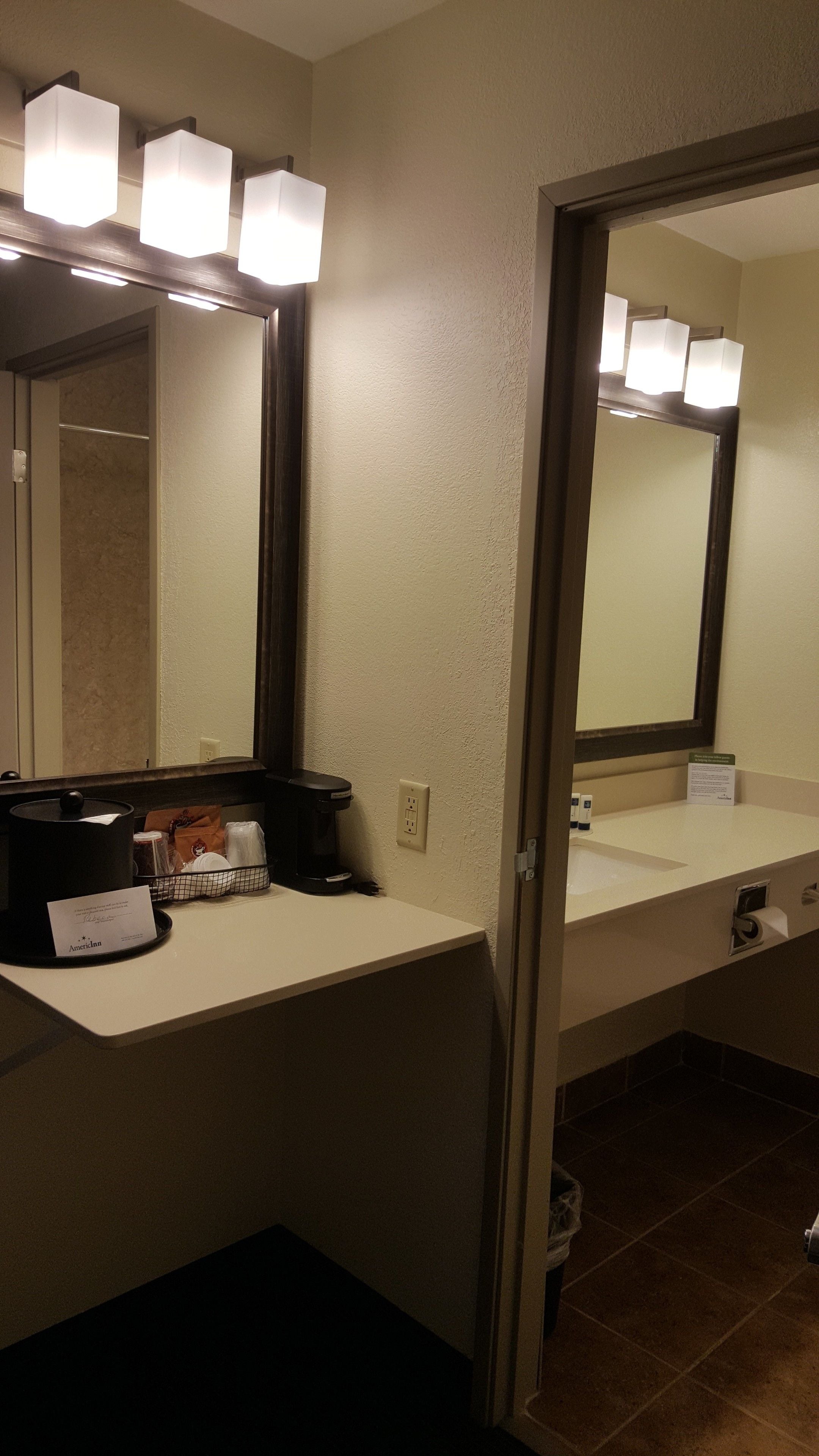 A hotel bathroom with a vanity, a large mirror, and three illuminated lights above the mirror.