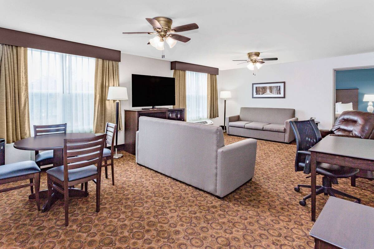 Habitación de hotel con comedor, sofá, televisor y dos ventiladores de techo.