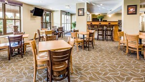 Un comedor de hotel con varias mesas y sillas de madera, una recepción y un ventanal que ofrece vistas al exterior.