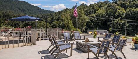 An outdoor seating area with chairs and a table, a flag, and a view of a forested hill.