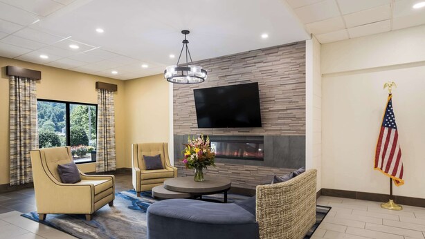 A modern living room with a flat-screen TV, comfortable seating, a fireplace, and an American flag. - Clarion Pointe Sylva near Cherokee Area (Sylva)