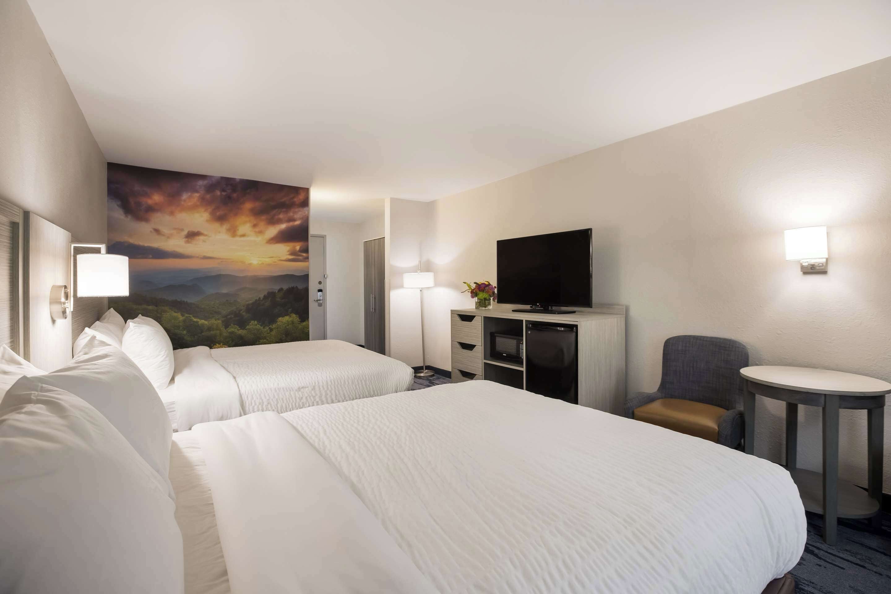 A hotel room with two beds, a TV, a desk, and a chair.