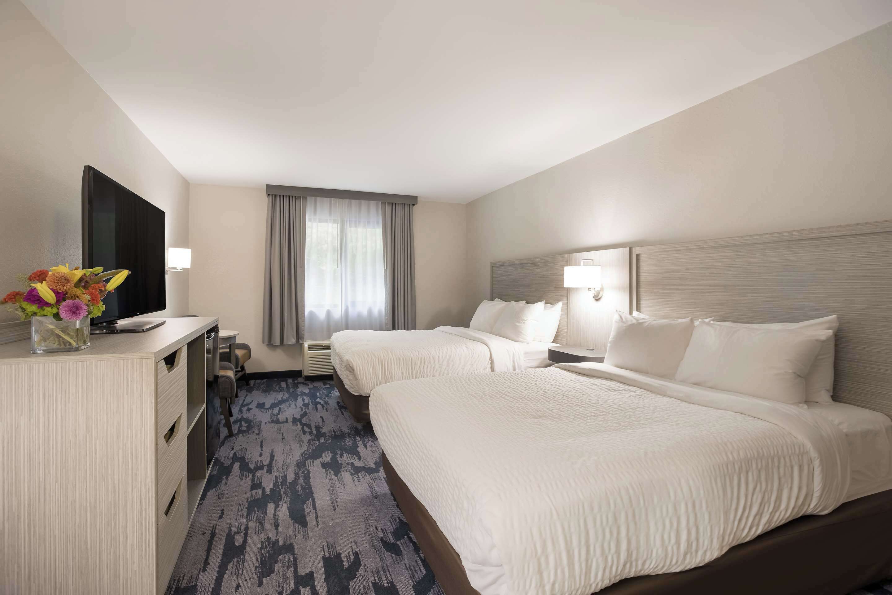 A hotel room with two beds, a desk, a TV, and a window with curtains.