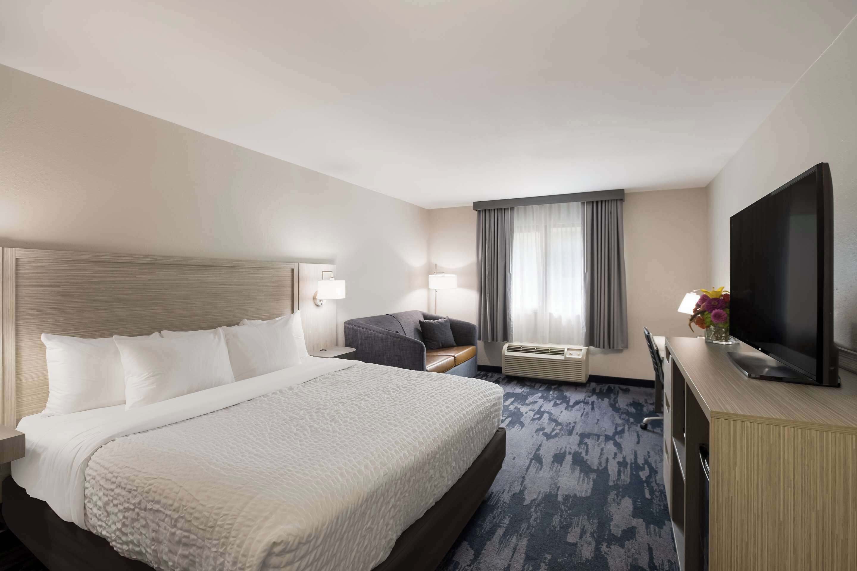 Habitación de hotel con una cama grande, un escritorio con televisor de pantalla plana, un sofá y una ventana con cortinas.