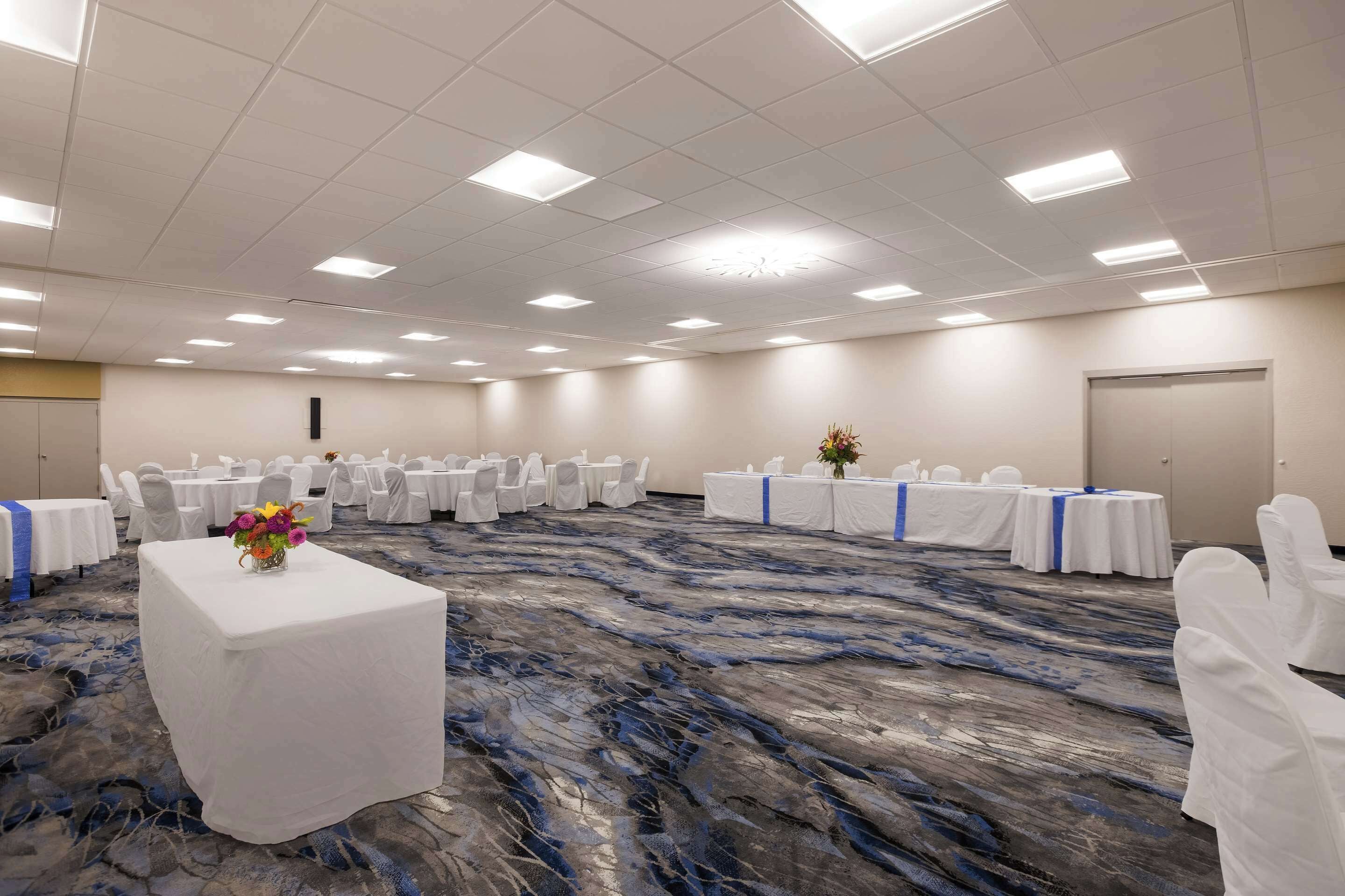 A large conference room with white tables and chairs, a marble-patterned carpet, and a ceiling with recessed lighting.