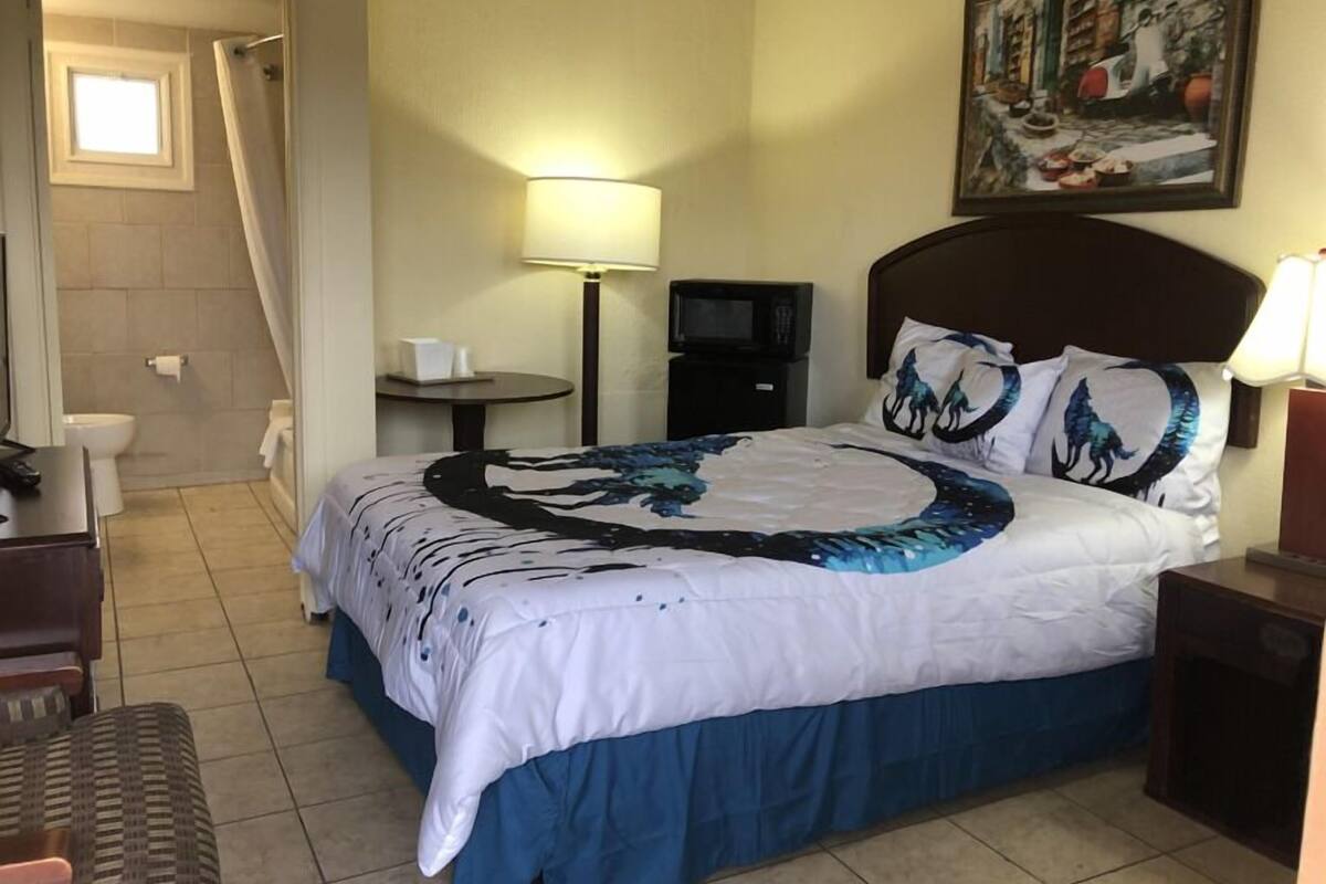 A hotel room with a bed, a desk, a chair, a TV, a painting, and a window.