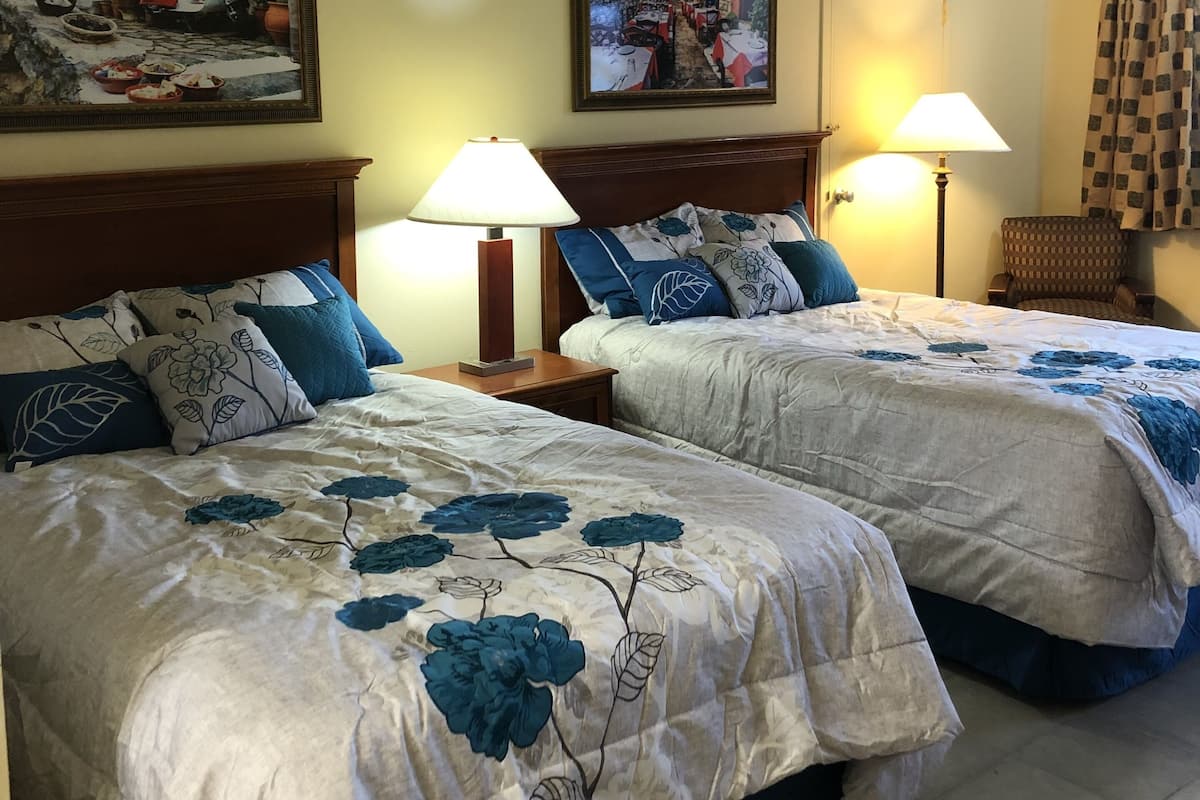 A hotel room with two beds, each with floral bedding and blue pillows, two bedside lamps, and two paintings on the walls.