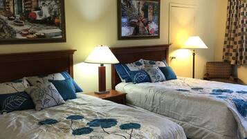 Habitación de hotel con dos camas, cada una con ropa de cama floral y almohadas azules, dos lámparas de noche y dos cuadros en las paredes.