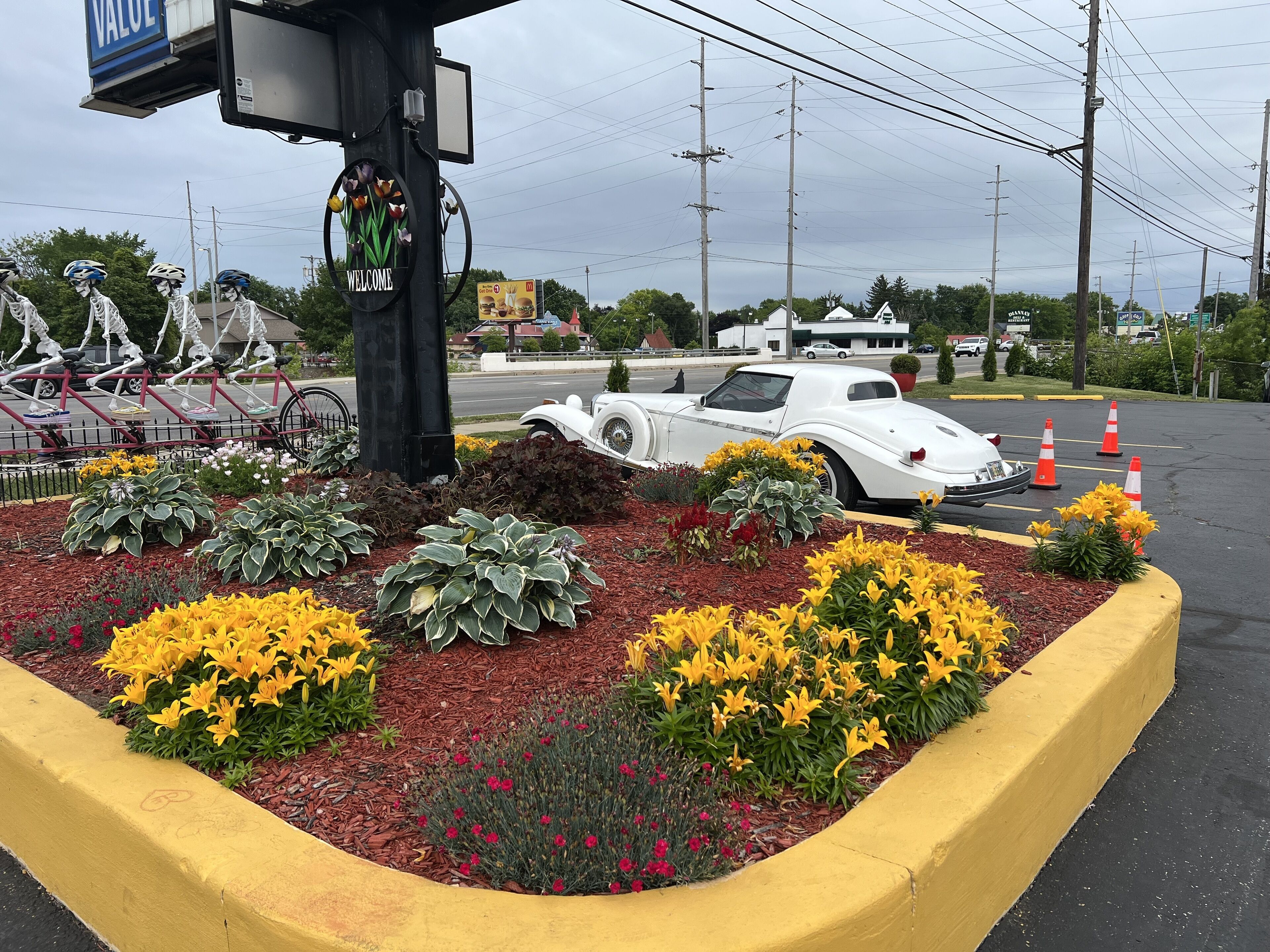 A parking lot with a white vintage car, a 'WELCOME' sign, and a row of bicycles.