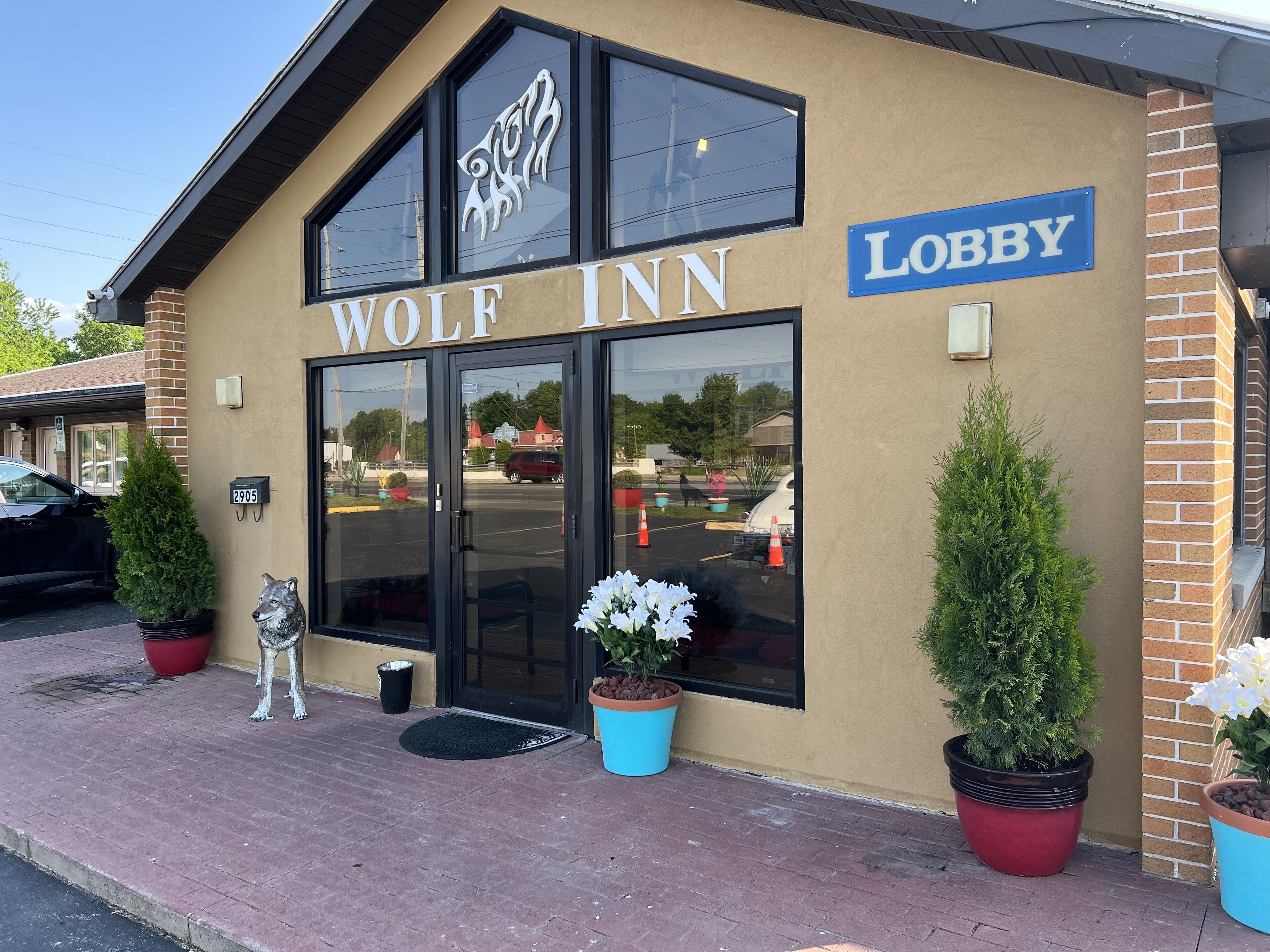 Ein Gebäude mit der Aufschrift "WOLF INN" und einem "LOBBY"-Schild, großen Fenstern und Topfpflanzen.