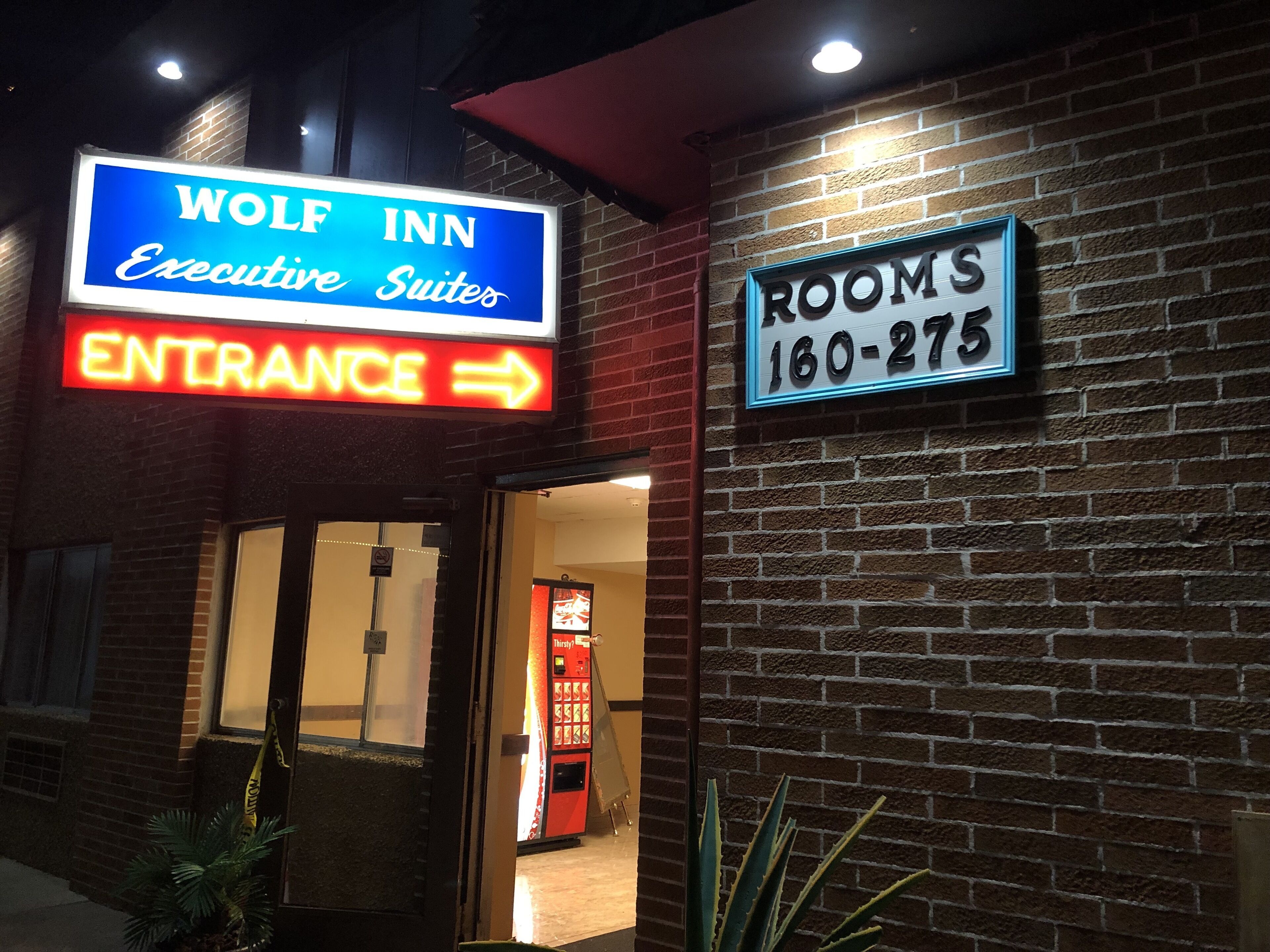 The exterior of the Wolf Inn, featuring a neon sign for the Executive Suites and a Rooms sign with a phone number.
