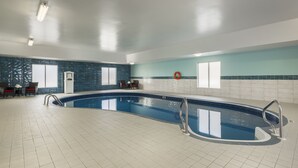 En stor swimmingpool indendørs med flisegulv, væg i blå og hvid samt et siddeområde med stole og bord.