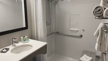 Un baño moderno con lavamanos, espejo y zona de ducha blancos.